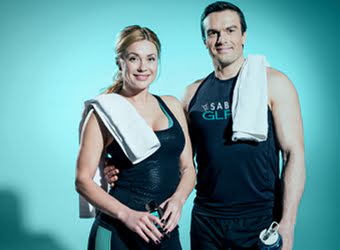 A man and woman in workout clothes with towels over their shoulders, standing together after exercise.